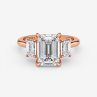Rose gold ring with emerald-cut diamond and baguette side stones on a white background