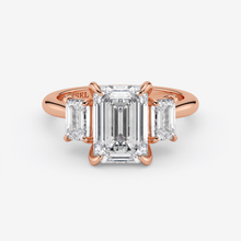 Rose gold ring with emerald-cut diamond and baguette side stones on a white background