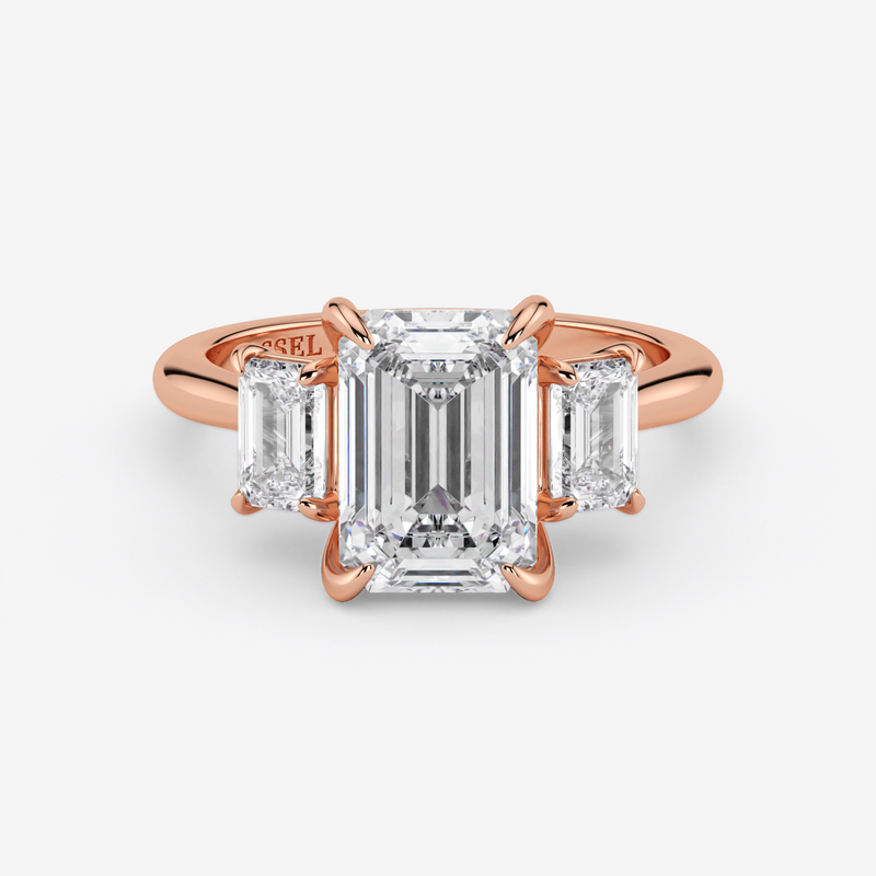 Rose gold ring with emerald-cut diamond and baguette side stones on a white background
