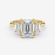 Gold ring with emerald-cut diamond and two side stones on a white background