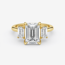Gold ring with emerald-cut diamond and two side stones on a white background