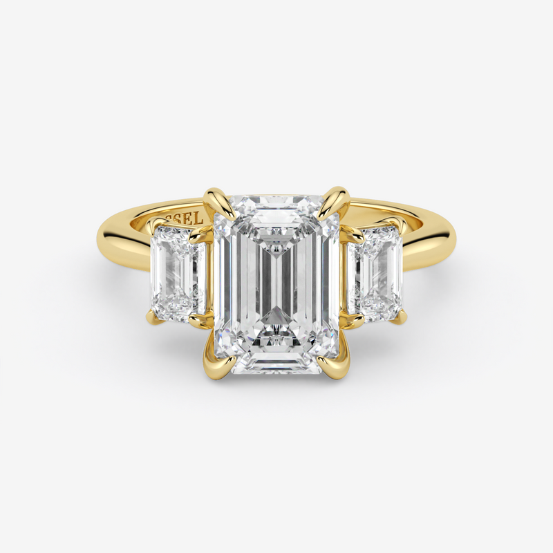 Gold ring with emerald-cut diamond and two side stones on a white background