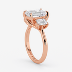 Rose gold ring with emerald-cut diamonds on a white background