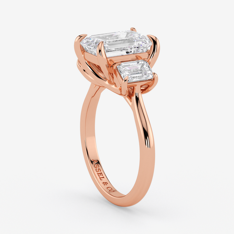 Rose gold ring with emerald-cut diamonds on a white background