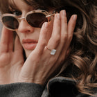 Woman wearing sunglasses and a ring with a Assel and Co diamond, close-up of face and hand.