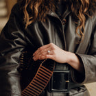Person wearing a dark leather jacket with a fur-lined hood, holding a brown and black striped bag.