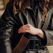 Person wearing a dark leather jacket with a fur-lined hood, holding a brown and black striped bag.