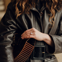 Person wearing a dark leather jacket with a fur-lined hood, holding a brown and black striped bag.